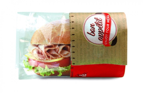 Opakowanie Snack Bag M NATURE Fifty Fifty w przezroczystym folii, z nadrukiem bon appétit i ENJOY YOUR MEAL. W środku widoczny kanapka z szynką, serem, sałatą i pomidorem. Ułożone z boku, z czerwonym dolnym paskiem.