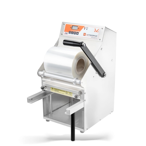 Zgrzewarka ręczna METROOPACK TSM 102-R bez matrycy, w kolorze metalicznym, z rolką przezroczystej folii. Ujęcie frontalne pokazuje uchwyt do podnoszenia oraz panel sterujący z wyświetlaczem. W dolnej części widoczne są elementy do mocowania pojemników.